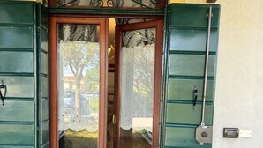 Una puerta de madera con contraventanas verdes, un pequeño porche y un felpudo.