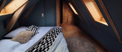 A bedroom with a sloped ceiling, wooden beams, and skylights.