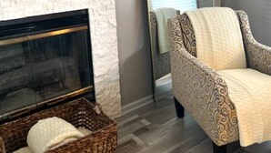 A living room with a fireplace, a mirrored wall, a patterned armchair, and a wicker basket.