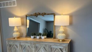 A wooden cabinet with two lamps, a mirror, and small potted plants.