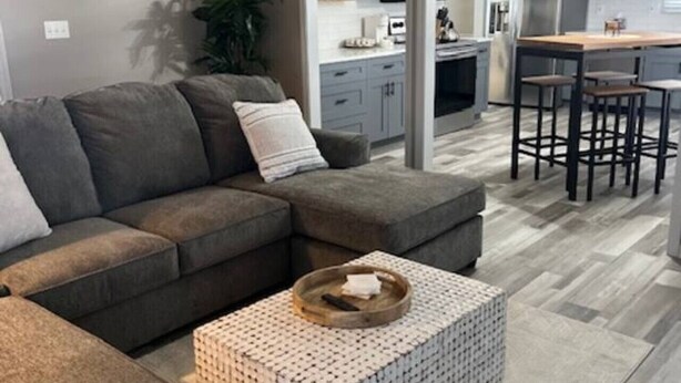 A modern living room with a sectional sofa, a patterned ottoman, and a kitchen in the background.