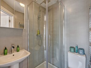 Un baño moderno con ducha envuelta en vidrio, un lavamanos blanco y artículos de aseo en la encimera.