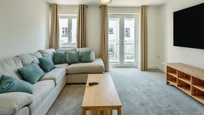 A modern living room with a sectional sofa, a wooden coffee table, and a TV mounted on the wall. - 3 bedroom accommodation in Paignton (Paignton)