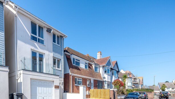 A row of two-story houses with attached garages, a clear blue sky, and a street with parked cars. - 3 bedroom accommodation in Paignton (Paignton)