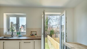 A modern kitchen with a large window, a wooden bench, and a view of a backyard. - 3 bedroom accommodation in Paignton (Paignton)