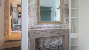 A hallway with a stone wall, a green cabinet, a fireplace with a decorative metal grate, and a hanging light fixture.