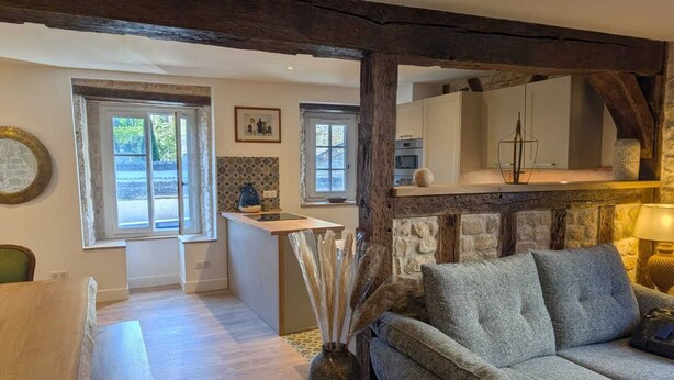 A cozy living room with a fireplace, a sofa, and a kitchen area in the background.