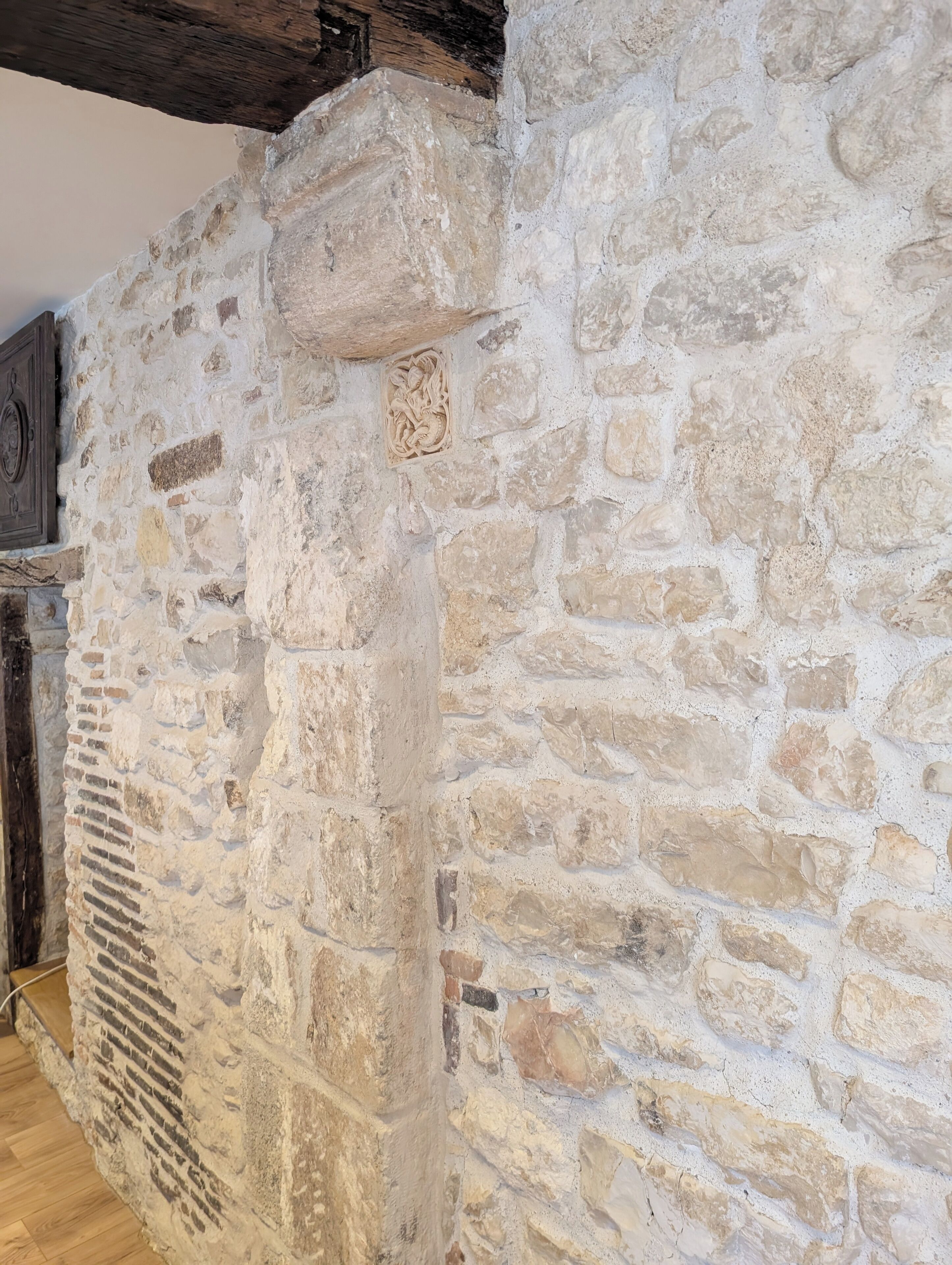 A stone wall with a decorative carving, a wooden beam ceiling, and a vent.