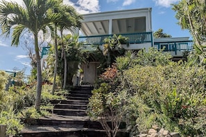 Ein Gebäude mit weißer Fassade und blauen Akzenten, umgeben von üppiger Vegetation und Palmen.