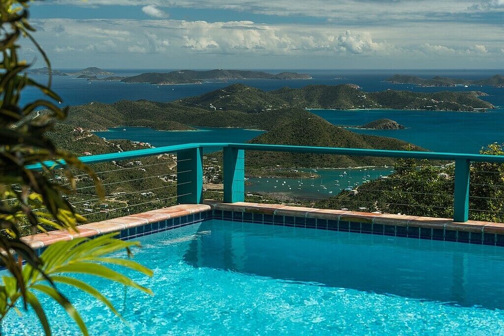 En swimmingpool med himmelblå gelænder, omgivet af frodigt grønt og med udsigt over idylliske øer og havet.