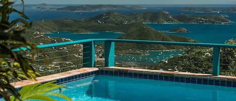 En swimmingpool med himmelblå gelænder, omgivet af frodigt grønt og med udsigt over idylliske øer og havet.