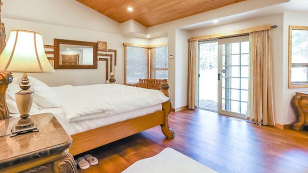 A spacious bedroom with a large bed, wooden flooring, a ceiling fan, and a sliding glass door leading to an outdoor area.