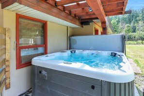 Una vasca idromassaggio esterna con una pergola in legno sopra, una finestra con persiane e vista su un paesaggio verde.