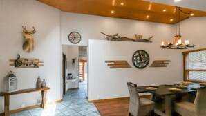 A dining area with a wooden table and chairs, a chandelier, and wall-mounted decor including a deer head and a clock.