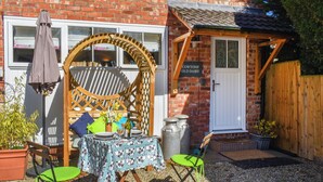 A patio with a table set for two, surrounded by chairs, a wooden arbor, and a small garden area with plants and a wooden fence. - 1 bedroom accommodation in East Cowton (East Cowton)