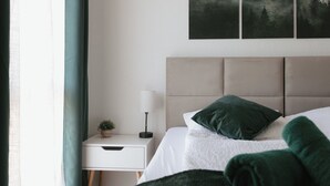 Et pænt og ryddeligt soveværelse med seng, puder, et natbord med lampe og en lille plante.