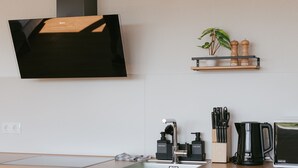 Et moderne køkken med et fladskærms TV på væggen, en træhylde med køkkenudstyr, en kaffemaskine og en vask med sæbedispensere.