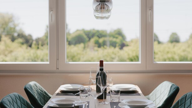 Et spisebord dækket til fire personer med vin, glas og tallerkener, med udsigt over en vingård.