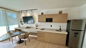 Une cuisine moderne avec des meubles en bois, un réfrigérateur en acier inoxydable, un téléviseur à écran plat et un coin repas avec des chaises en osier.