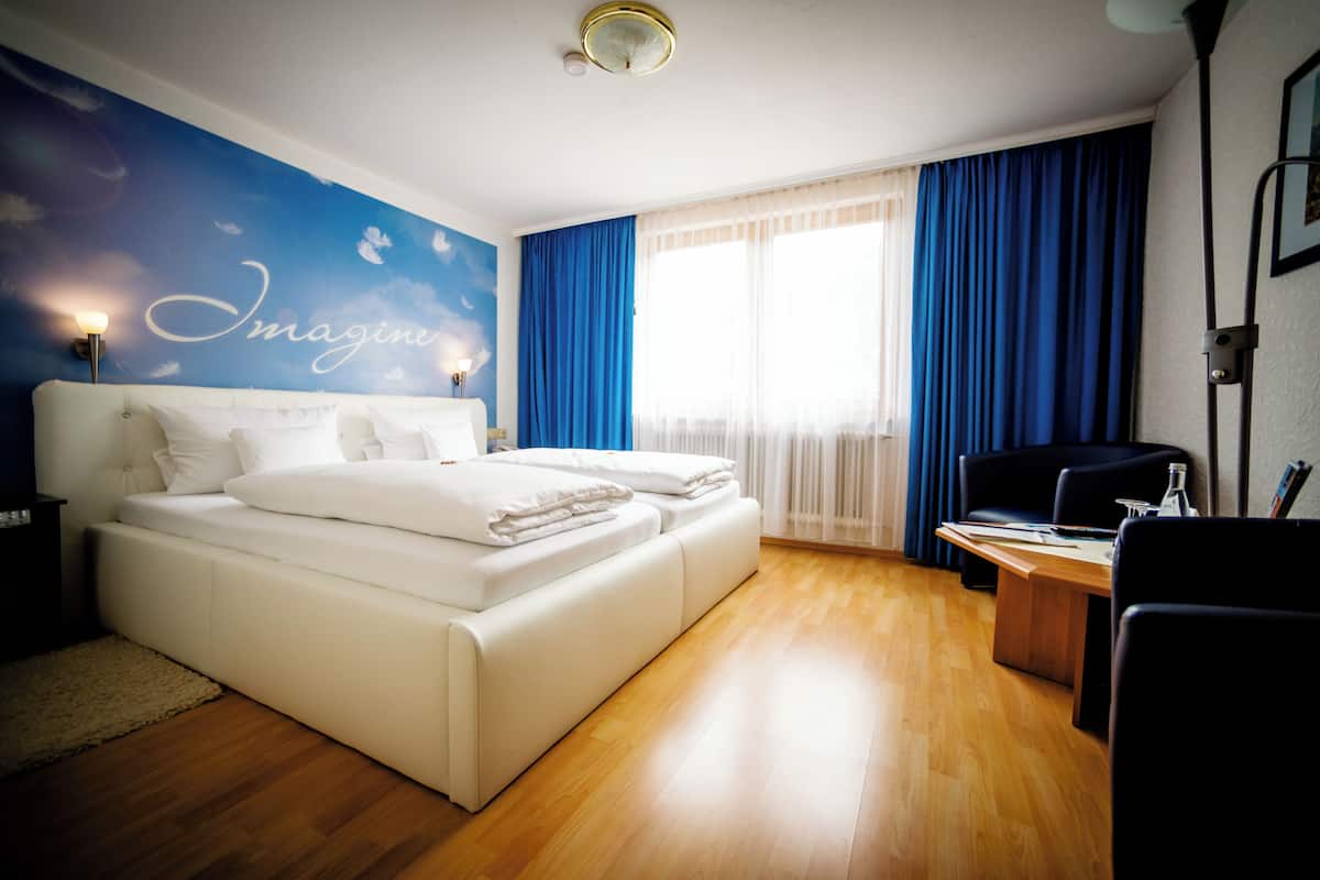 A modern hotel room with a large bed, a desk, and a view of the outdoors through the window.