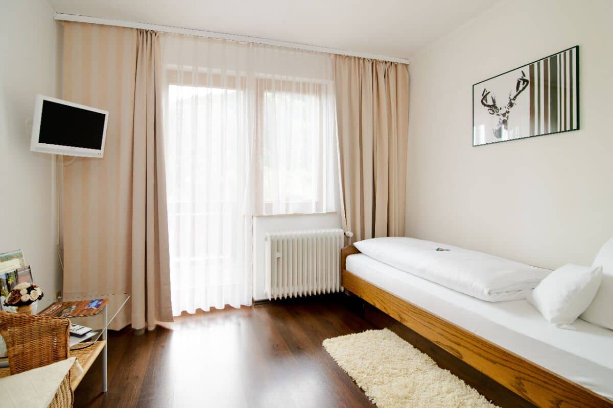 A bedroom with a bed, a TV, a radiator, and a window with curtains.