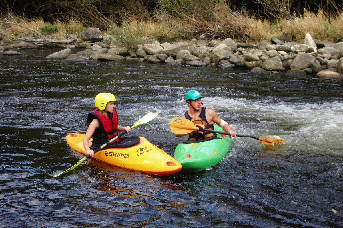 Dos personas remando en kayak por un río.