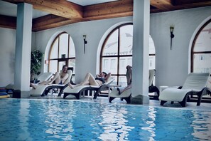 A pool area with lounge chairs and a view of the outside through large arched windows. - Holzschuh Schwarzwaldhotel (Baiersbronn)