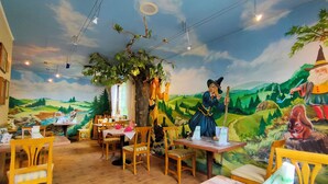A restaurant with wooden furniture, a mural of a forest scene, and a dining table set with plates and cutlery. - Holzschuh Schwarzwaldhotel (Baiersbronn)