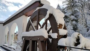 A snow-covered wooden structure with large wheels, likely a historical water mill, surrounded by snow-laden trees. - Holzschuh Schwarzwaldhotel (Baiersbronn)