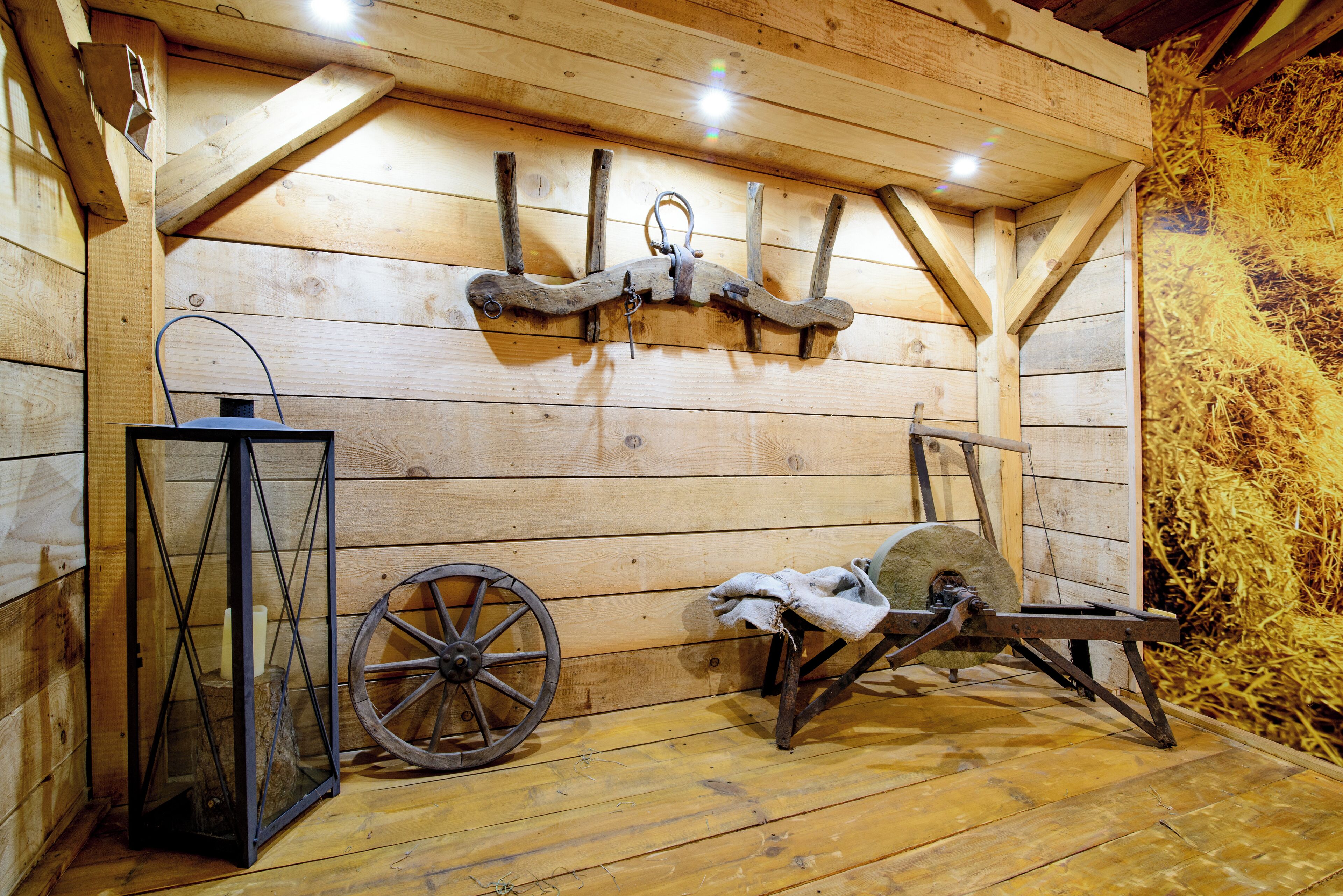 A rustic wooden room with a wooden ceiling, a wheel, a wooden bench, and a lantern.