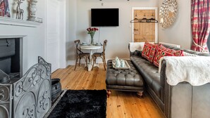 A living room with a fireplace, a dining table with chairs, a sofa, and a TV mounted on the wall. - Escape to our luxury cottage in Ganton, near Scarborough. (Ganton, near Scarborough)