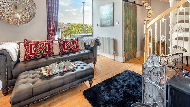 A spacious living room with a leather sofa, a large window, and a staircase with ornate railings. - Escape to our luxury cottage in Ganton, near Scarborough. (Ganton, near Scarborough)