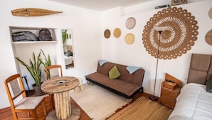 A cozy room with a brown sofa, wooden chairs, a round wooden table, and a small shelf with bags. - Alojamiento en Centro Histórico Cusco (Cusco)