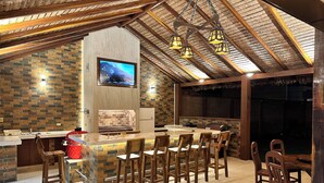 A kitchen with a brick backsplash, wooden ceiling beams, and a TV mounted on the wall. - Seasonal House (Santa Cruz de la Sierra)