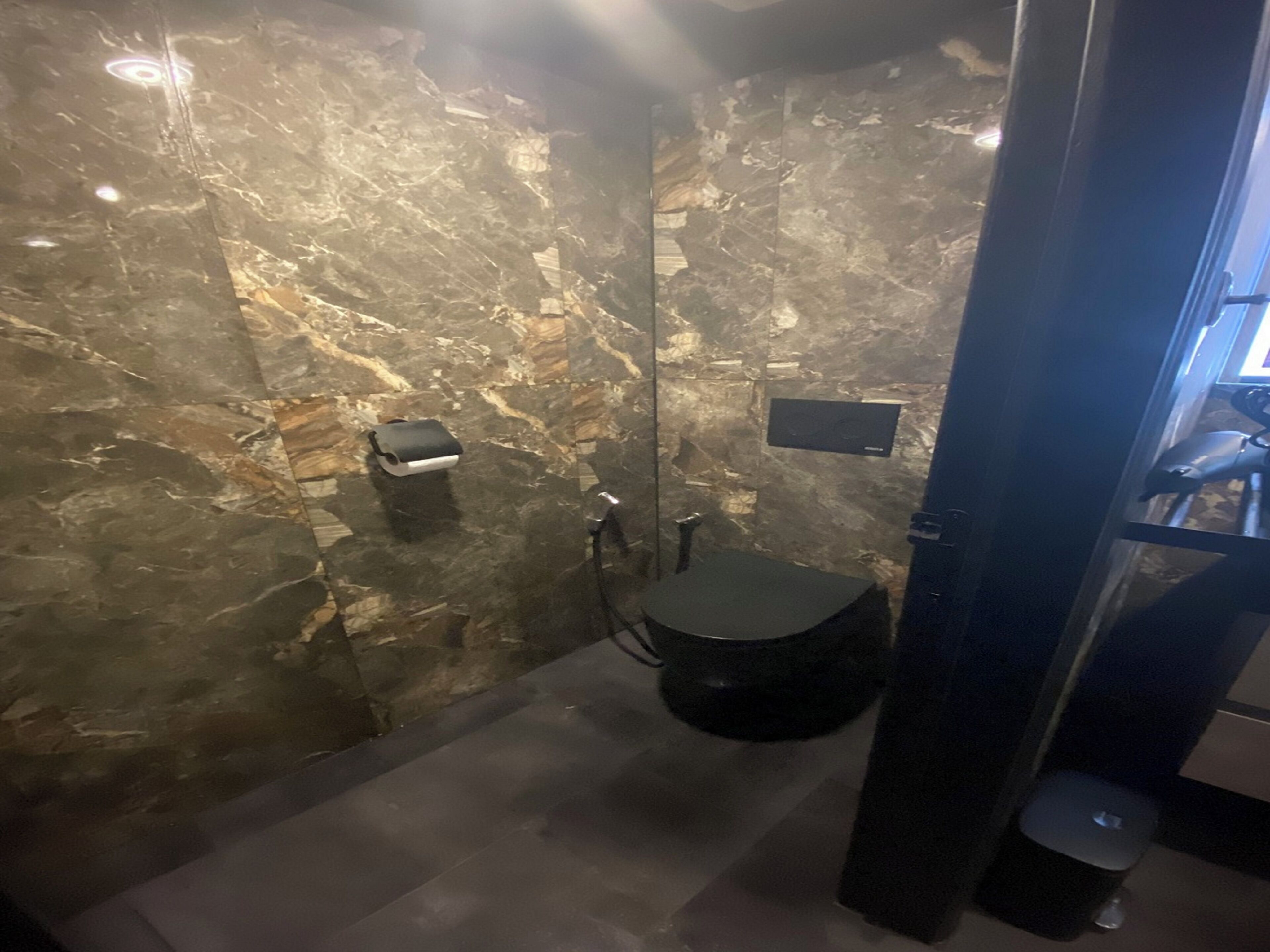 A bathroom with a marble wall, a black sink, and a handheld showerhead.