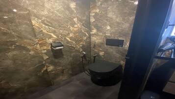 A bathroom with a marble wall, a black sink, and a handheld showerhead.