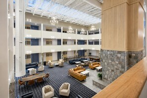 Un vestíbulo de hotel de varios niveles con techo alto, candelabros y mesa de billar.