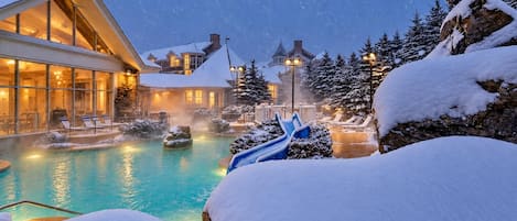 A resort with a heated pool, lounge chairs, and snow-covered trees.