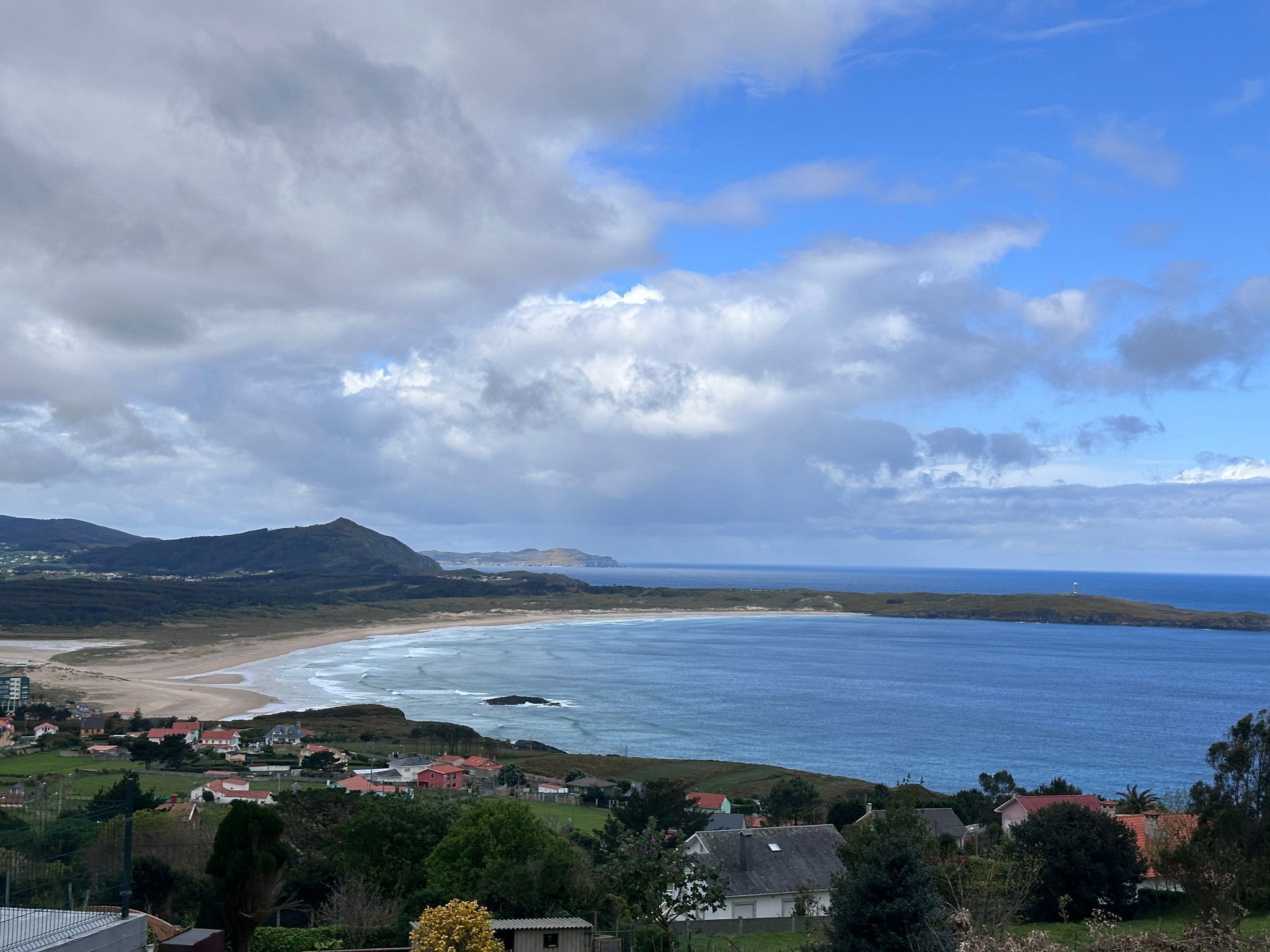 A coastal landscape with a beach, ocean, and hills in the background.