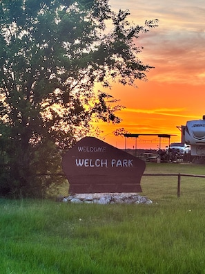 A welcome sign at Welch Park with a sunset in the background.