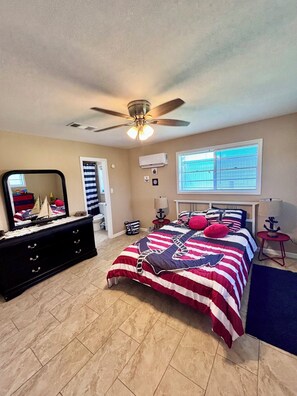 Une chambre à coucher comprenant un lit, une commode, un ventilateur de plafond, un appareil de climatisation et une fenêtre avec des stores.