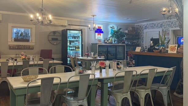 Interior de restaurante con suelos de madera, sillas y mesas de metal, un letrero de neón y un refrigerador.