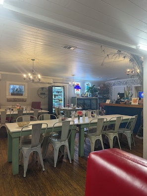 L’intérieur d’un restaurant avec un sol en bois, des chaises et des tables en métal, un panneau lumineux au néon et un réfrigérateur.