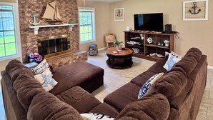 Una sala de estar con chimenea, ventilador de techo, televisor y un conjunto de sofás.