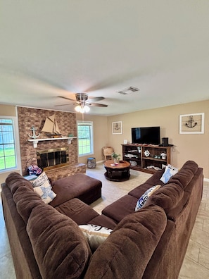 A living room with a fireplace, a ceiling fan, a television, and a sofa set.