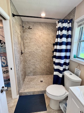 A bathroom with a shower, toilet, and a window.