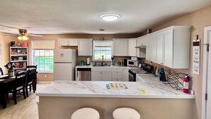 Una cocina con una isla de mármol, dos taburetes de bar, una mesa de comedor con sillas y un refrigerador.