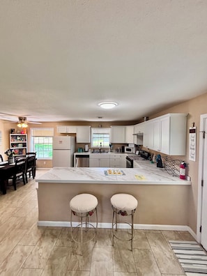 A kitchen with a marble island, two bar stools, a dining table with chairs, and a refrigerator.