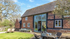 A brick house with a glass extension, outdoor seating, and a lawn.