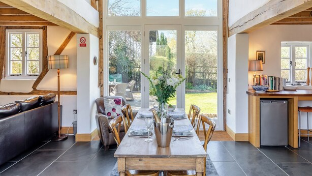 A dining area with a wooden table, chairs, and a view of the garden through large windows.